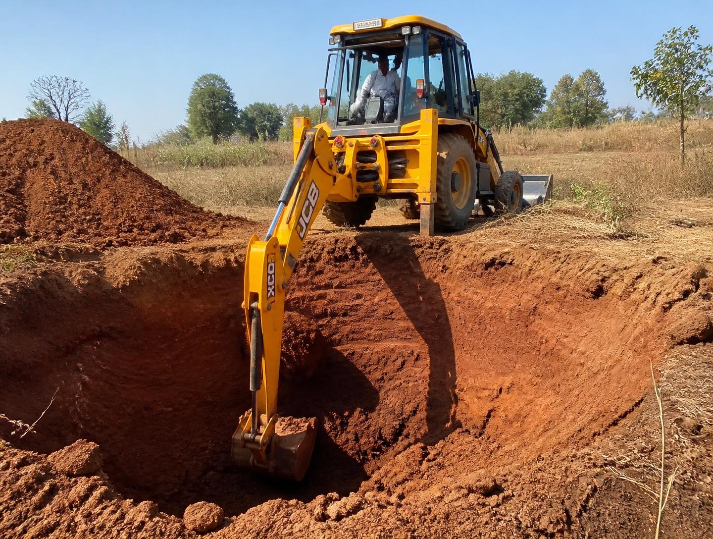 Heavy JCB machinery excavating an open well site with an operator in the cabin